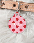 Pink polka dot dog tag with 'TULLY' on a beige leather collar on a white fur background