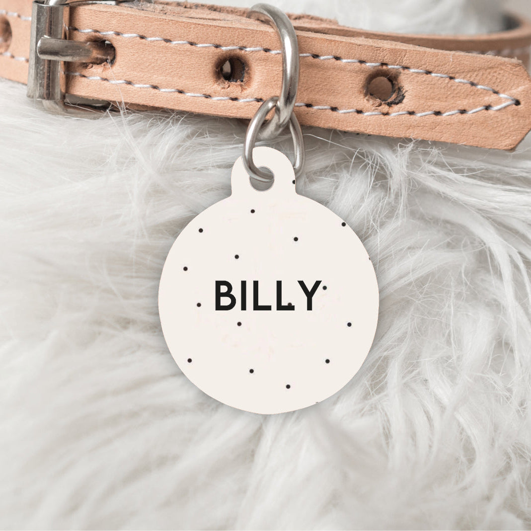 Dog collar with a pink leather strap and a round metal tag engraved with 'BILLY' on a fluffy white background.