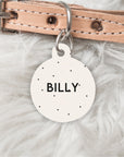 Dog collar with a pink leather strap and a round metal tag engraved with 'BILLY' on a fluffy white background.